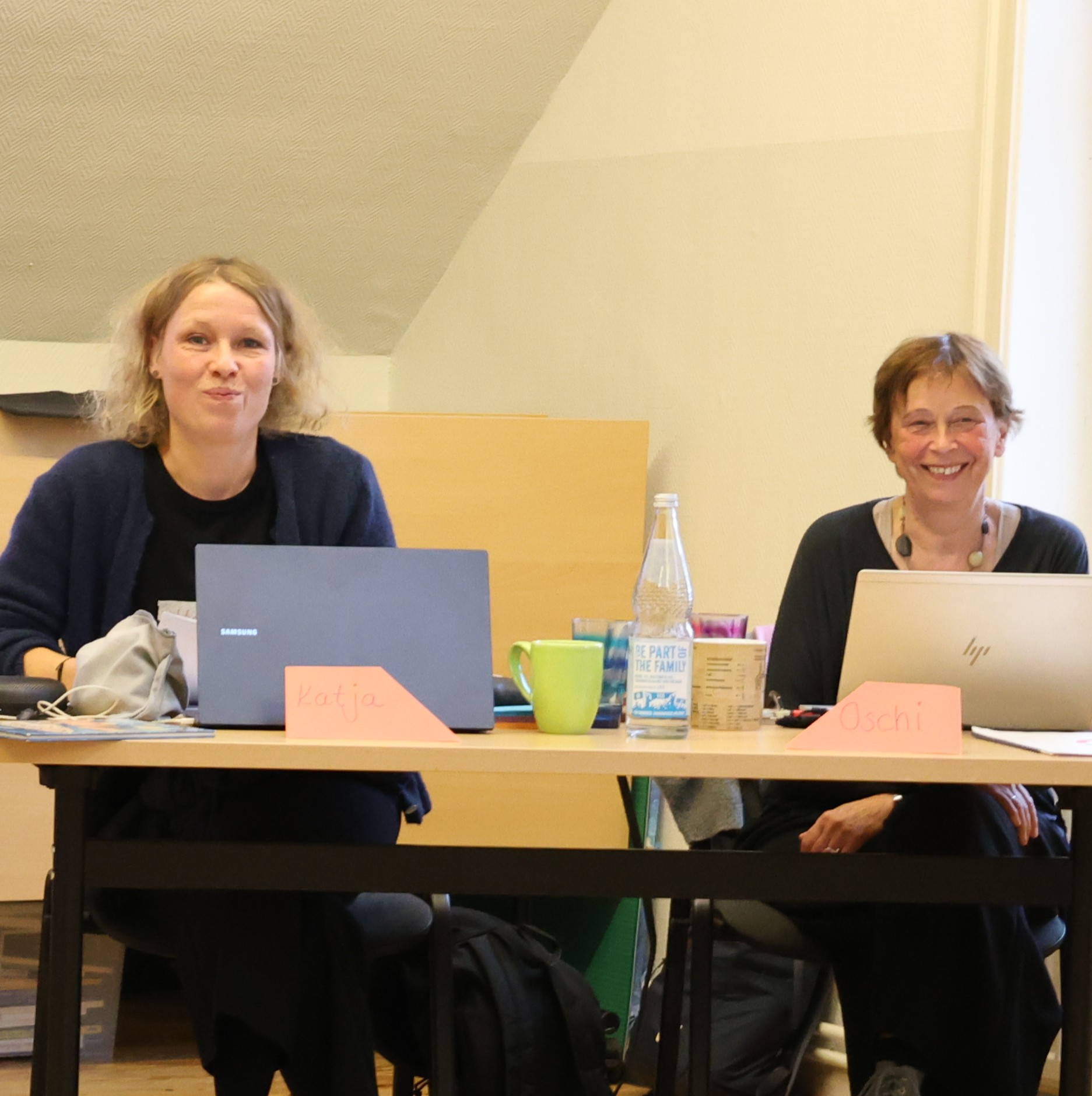 Zwei Frauen sitzen am Tisch mit Laptops.