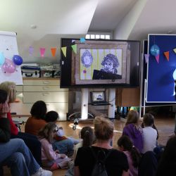 Kinder und Erwachsene sitzen auf dem Boden und schauen ein Video auf dem Boden und schauen ein Video auf dem Smartboard